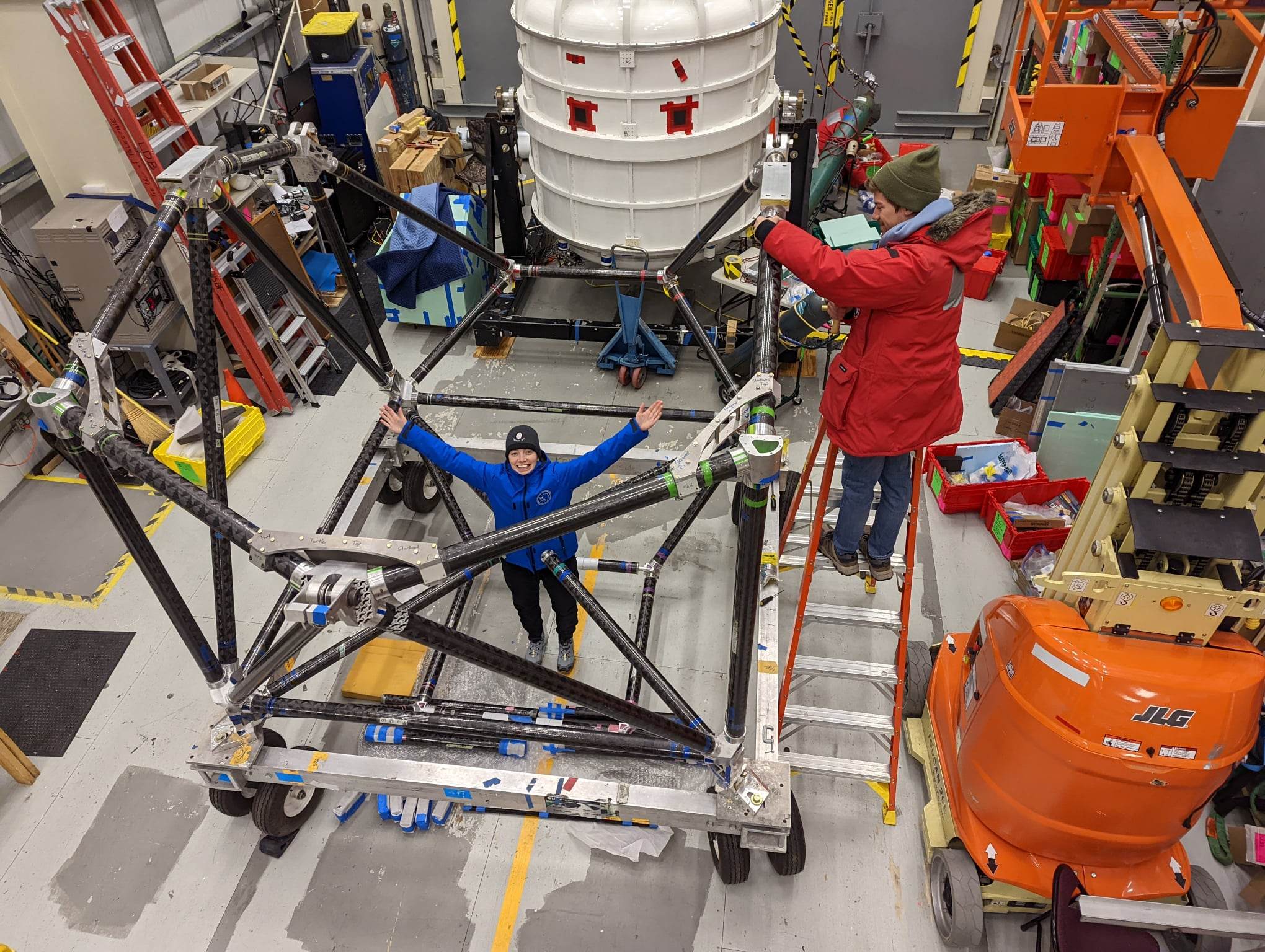 The cryostat (white cylinder in the background) is supported and controlled by an aluminum and carbon-fibre frame. In this image Susan Redmond is standing where the reaction wheel gets mounted. The reaction wheel uses angular momentum and enables scanning of the telescope.

PHOTO: SUBMITTED