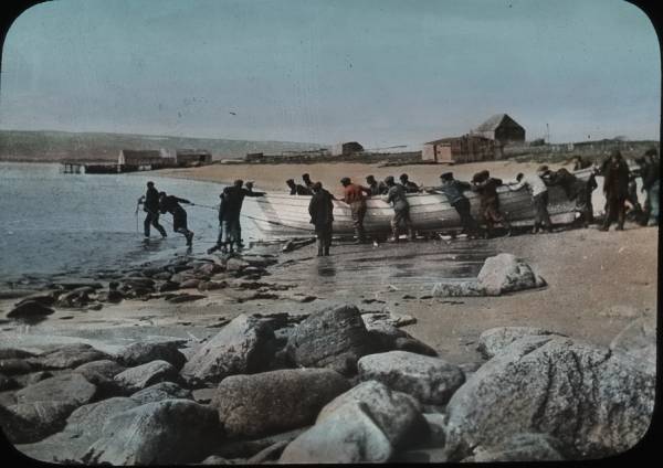 Many men dragging boat across sand to water, 1915