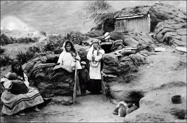 Women, children, and puppies in front of a sod house