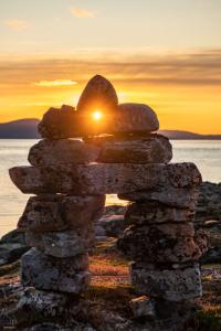 An inuksuk in front of a body of water, with the sun setting in the background