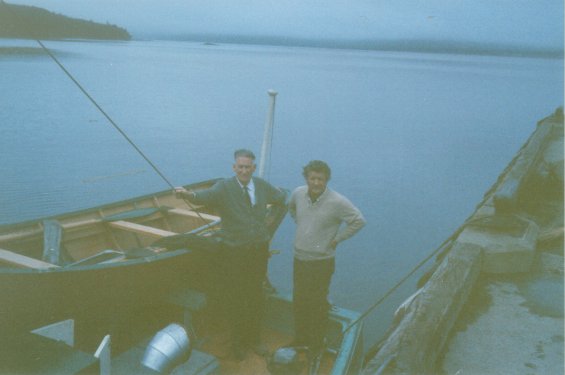 Harold L. Lake (right) with an unidentified man standing in a boat next to a wharf