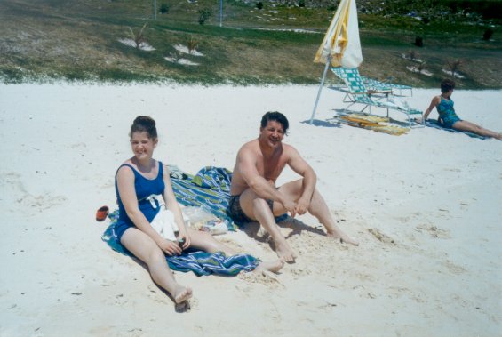 Harold L. Lake and his daughter sitting on a sandy beach in St. George, Bermuda
