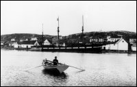 Boy rowing boat at Battle Harbour with the "Southern Cross" at the wharf