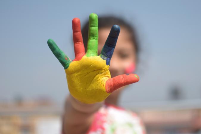 girl holding her hand with different coloured paint on fingers