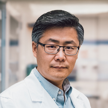 Portrait photo of Bing Chen wearing glasses and a white lab coat with a blurred background.