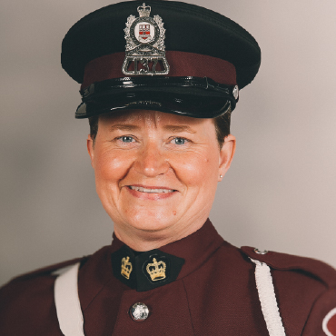 A head shot of Constance Fudge, a uniformed officer with Memorial University's Campus Enforcement and Patrol. She is smiling in a formal maroon dress uniform with a cap and white shoulder strap.