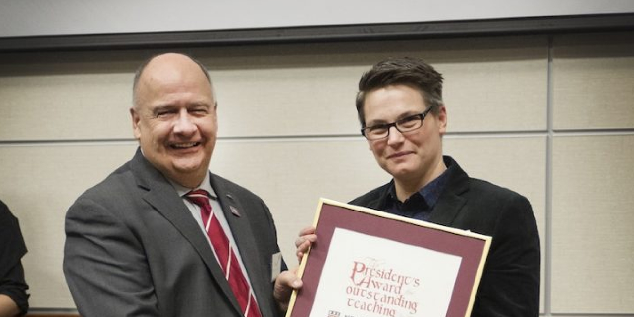 Former Memorial president Gary Kachanoski, wearing a suit and red striped tie, stands beside Ailsa Craig, who is dressed in a dark blazer and glasses. Dr. Craig holds a framed certificate for the President’s Award for Outstanding Teaching. Both are smiling during the award presentation.