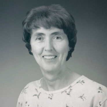 Black and white portrait of Elizabeth Miller smiling, wearing a light-colored top with a small floral pattern, posed against a plain studio background.