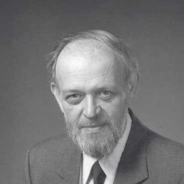 Black and white portrait of Fred Aldrich with a beard, wearing a suit and tie, facing the camera with a neutral expression.