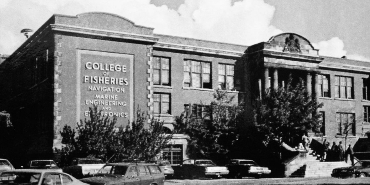 Black and white photograph of the historic brick building on Parade Street with its grand entrance featuring columns and decorative arch. A large sign on the side of the building reads, 