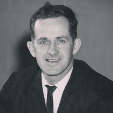 A black-and-white head shot of J. Douglas Eaton. He’s wearing a dark suit and tie and smiling.