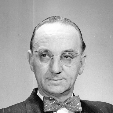 Black and white portrait of Joseph Smallwood wearing glasses, a suit, and a patterned bow tie, looking slightly to the side with a neutral expression.