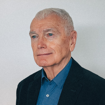 Portrait of Leslie O’Reilly wearing a dark blazer over a blue collared shirt, looking slightly to the side with a calm expression against a plain background.
