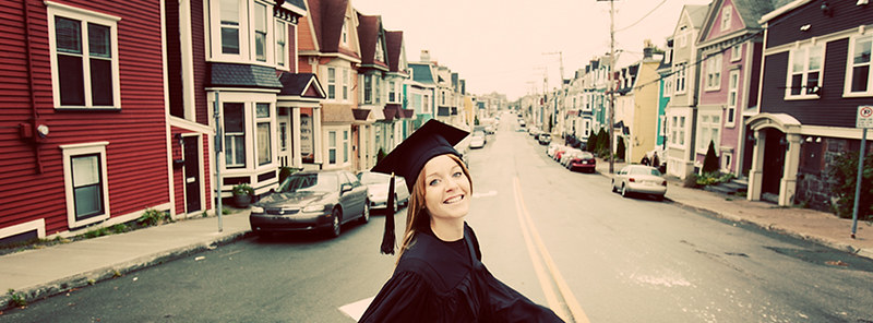 A student in their cap and gown smiling. Downtown St. John's is the background.