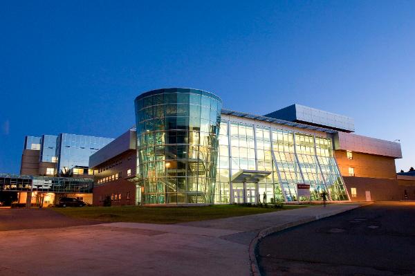 An exterior shot of the Bruneau Centre building on the St. John's campus of Memorial University. The shot is taken at dusk, with a dark-blue sky, and the building's glass facade is lit from inside.