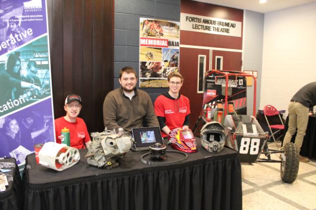 Three students sitting behind a table with a baja vehicle next to them.