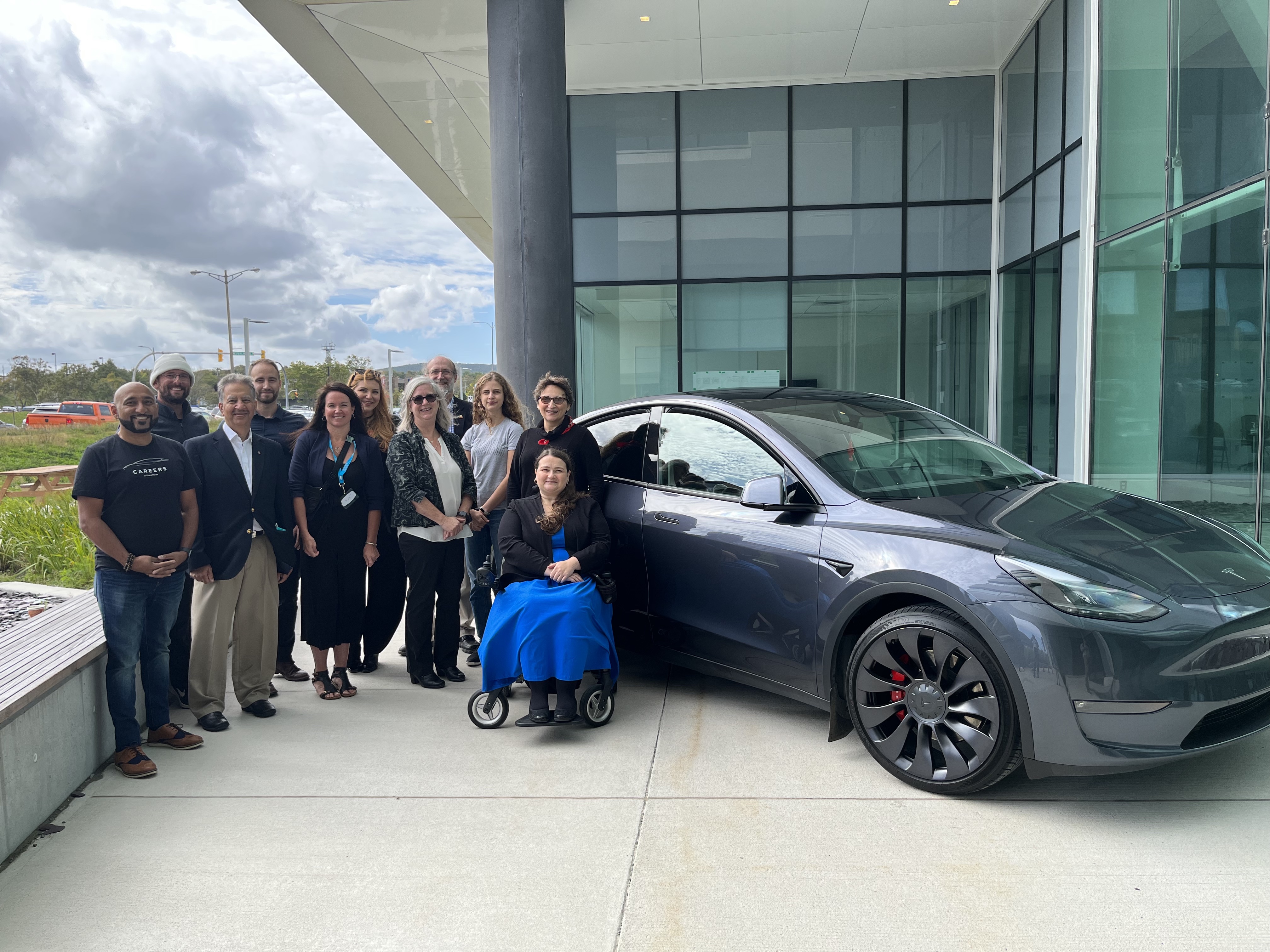 Members of Tesla's recruitment team and the Memorial community pose next to a Tesla vehicle.