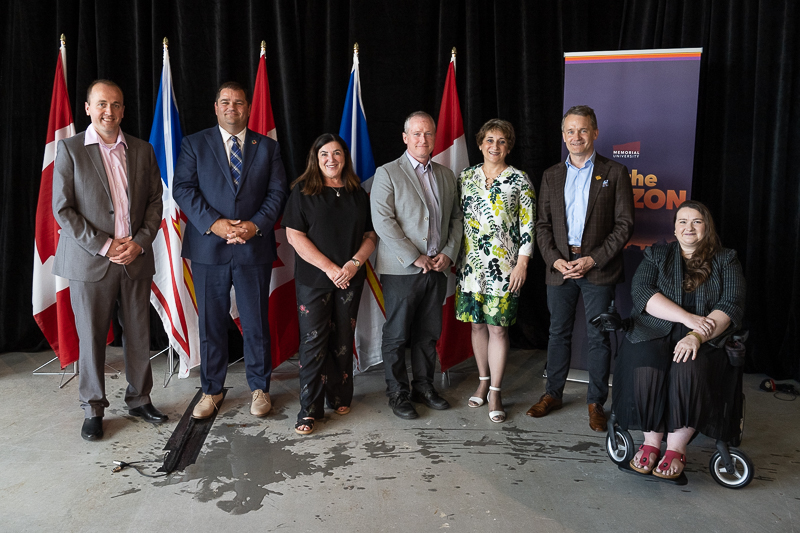 Seven people pose in front of federal and provincial flags