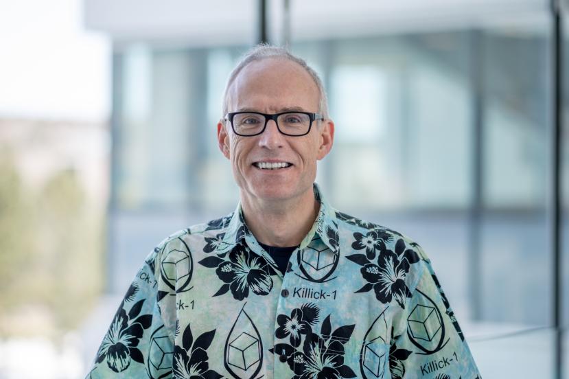 A man wearing a patterned shirt smiles at the camera.