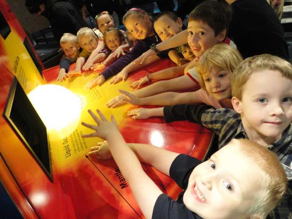 a group of smiling children surround a cut-away model of the Earth's core