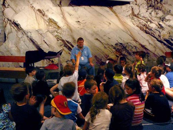 an interpreter sits in front of a natural rock wall, surrounded by young students