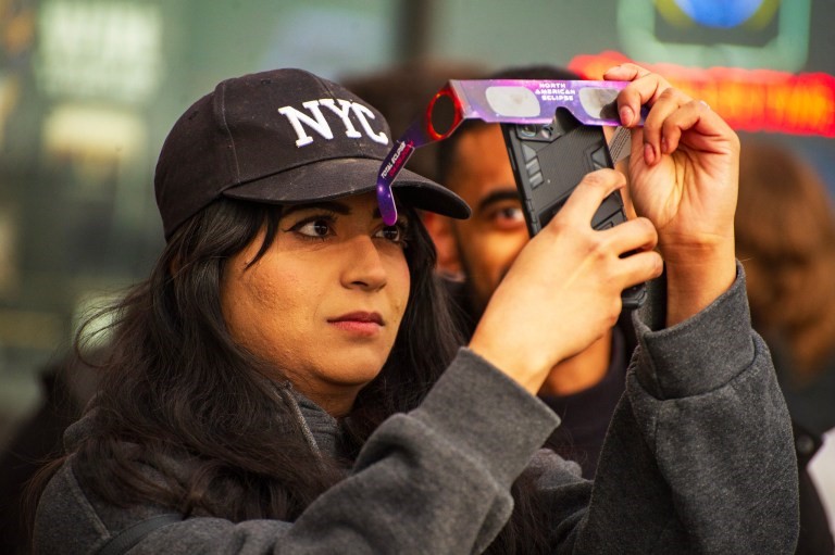 A woman uses protective glasses to protect her phone while taking a photo of the eclipse.