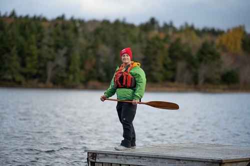 A photo of Dr. TA Loeffler standing on a dock wearing a life jacket and holding a canoe paddle.