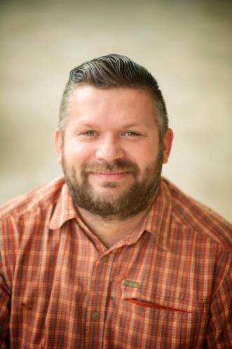 A smiling brown haired man with beard and orange shirt