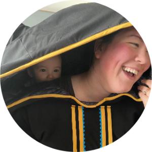Chelsea Flowers laughing and wearing her son, Kaleb, on her back under her hood.
