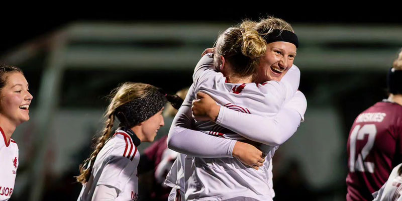 An action photo of two women's soccer student-athletes celebrating and embracing on the field
