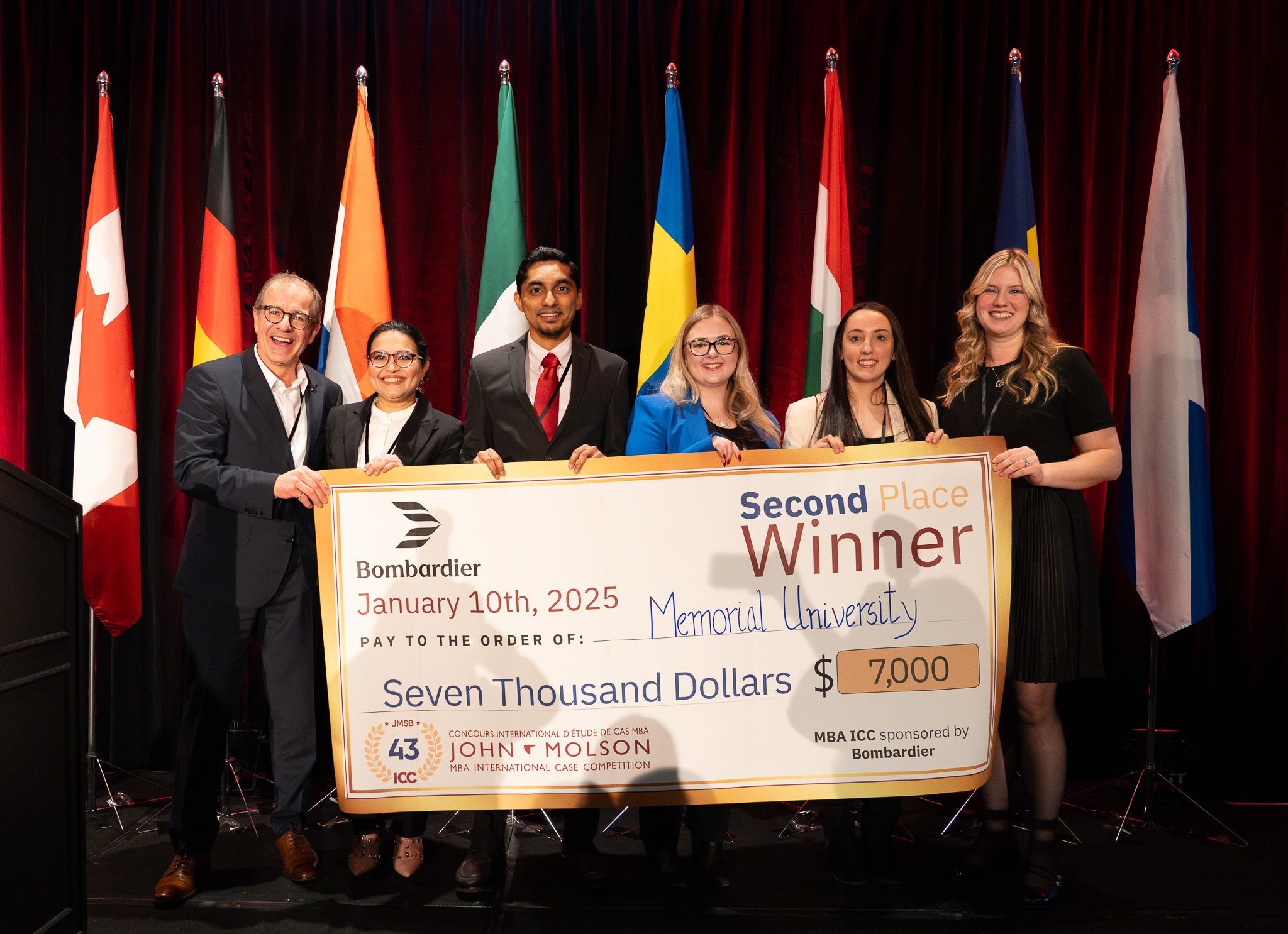A group of students holding an oversized cheque with flags behind them