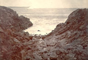 Unidentified rocky beach with ocean view and iceberg in background