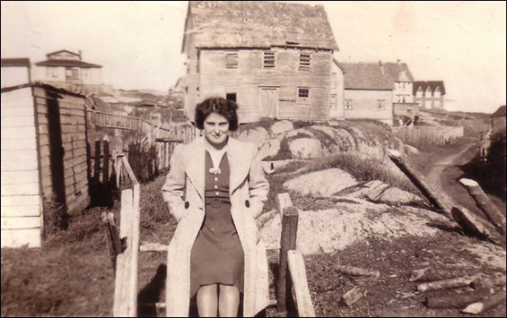  Elizabeth Feltham. Dilapidated house behind her was owned by Carrie King who left Deer Island for the U.S. after her husband was drowned in the schooner Little Jepp</em.