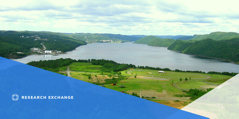 Photo of Miawpukek Mi'kamawey Mawi'omi First Nation reservation. The is a large grassy area, surrounded by a large river and lake within a valley.