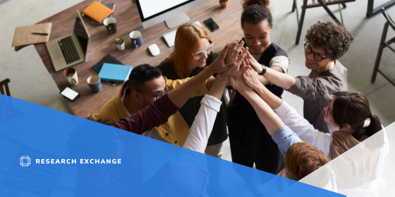 Photo of a group working together. They are raising their hands in the air together. 