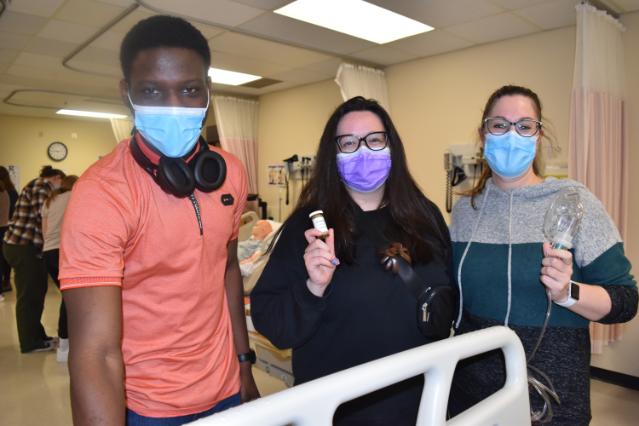 One male and two female students hold IV practice tools in the LRC