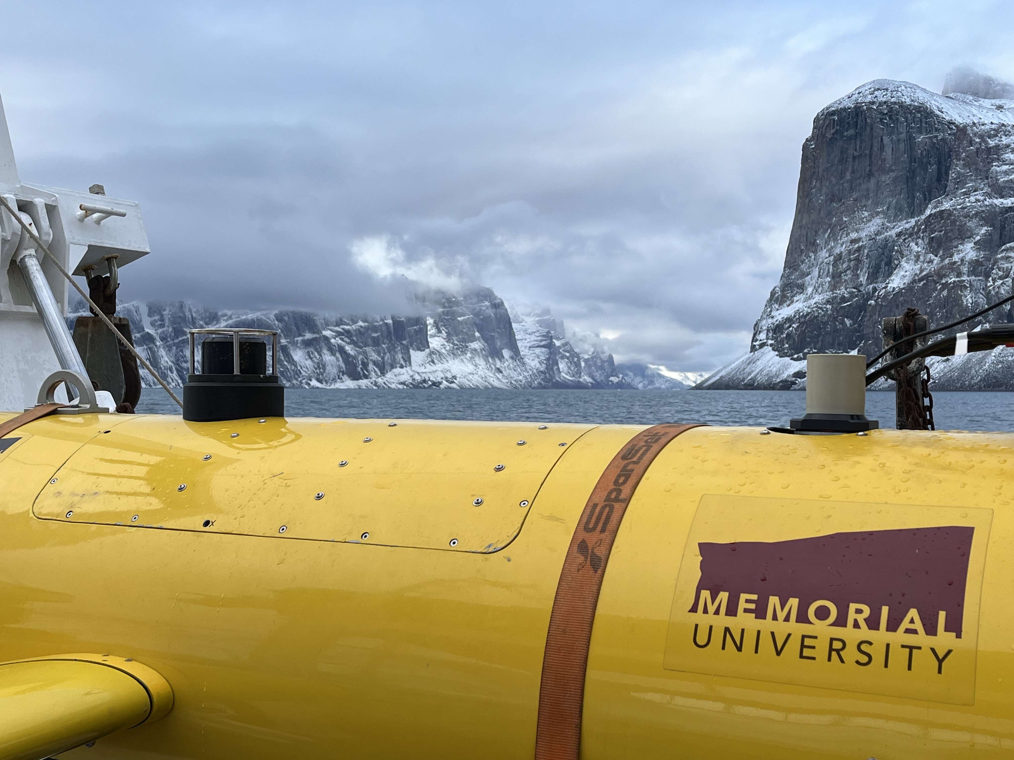 A yellow R.O.V. with Memorial's logo on the side, with the mountains and ocean in Baffin Bay in the background