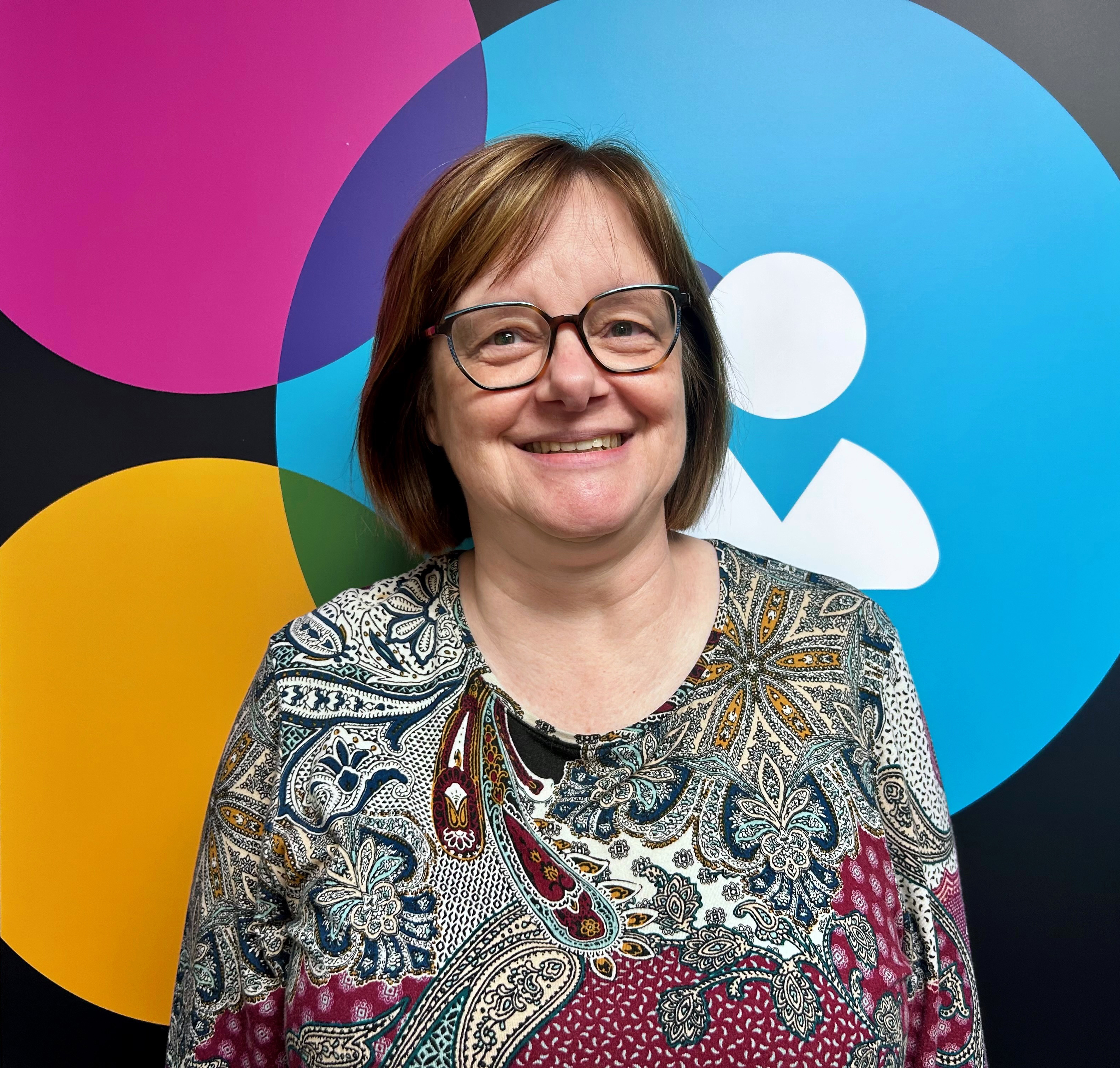 Photo of Cindy Maloney, a mom and pharmacist at the School of Pharmacy. Photo taken at the MTS Clinic in front of its logo.