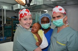 (L-R) Katie O’Brien, a Haitian anesthesiologist and Dr. Ed Redmond in November 2011. Katie is holding a baby who has just woken up following a cleft lip surgery.