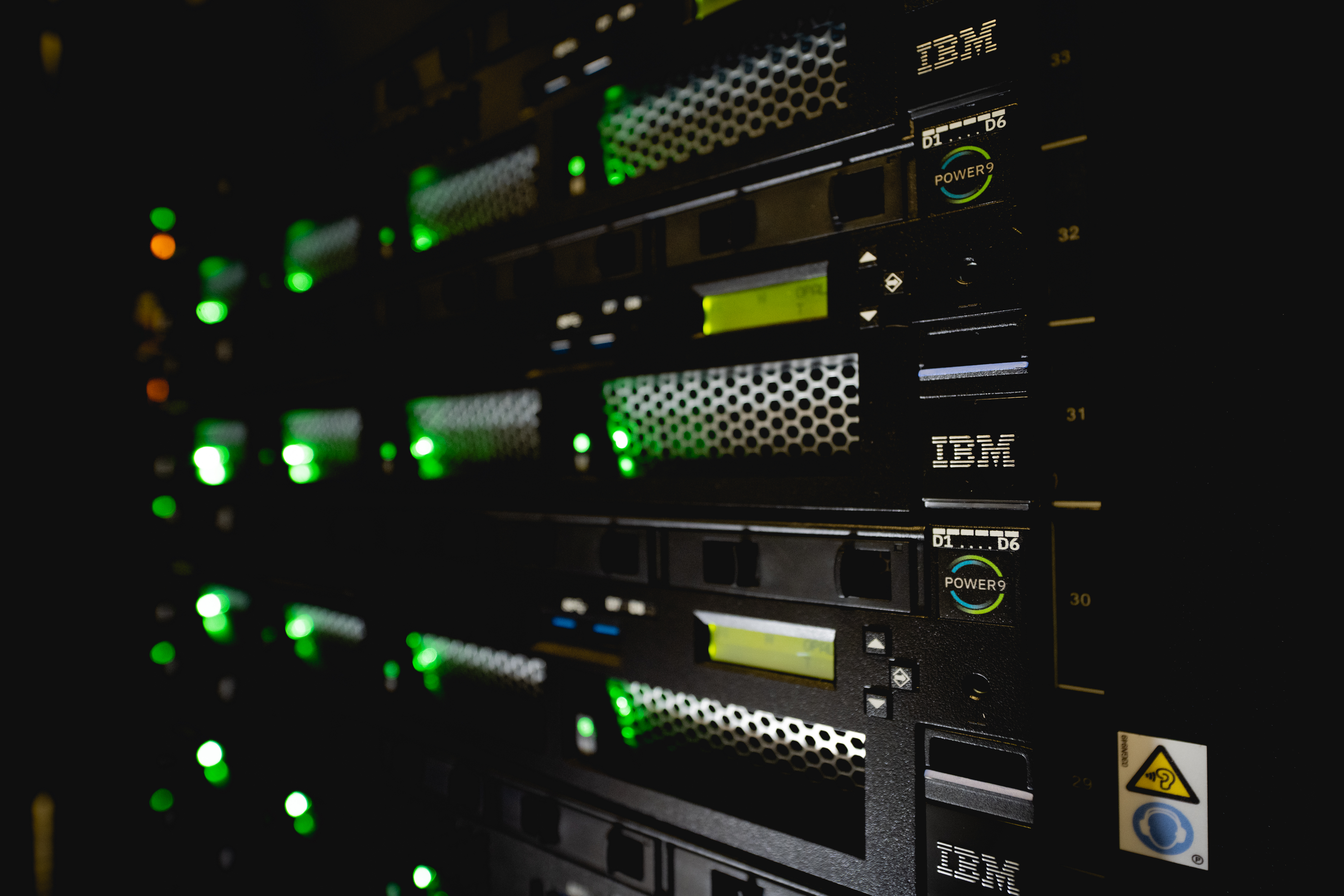A close up photo of computer servers in a dark room with green lights.