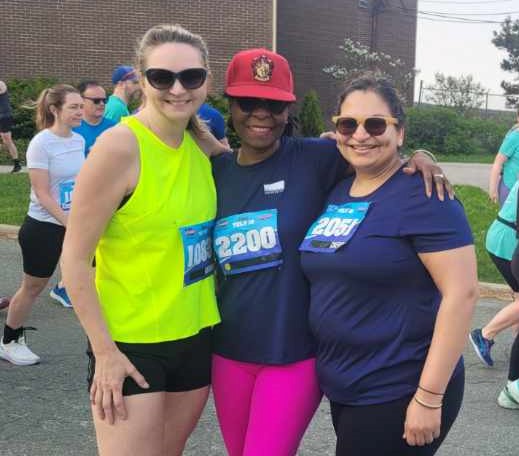 Three women -- from left to right, Roxanne Millan, Dr. Delores Mullings and Cherry Ralhan-Khanna -- wearing exercise clothing, race bibs and sunglasses are standing outside in a row next to each other and smiling.